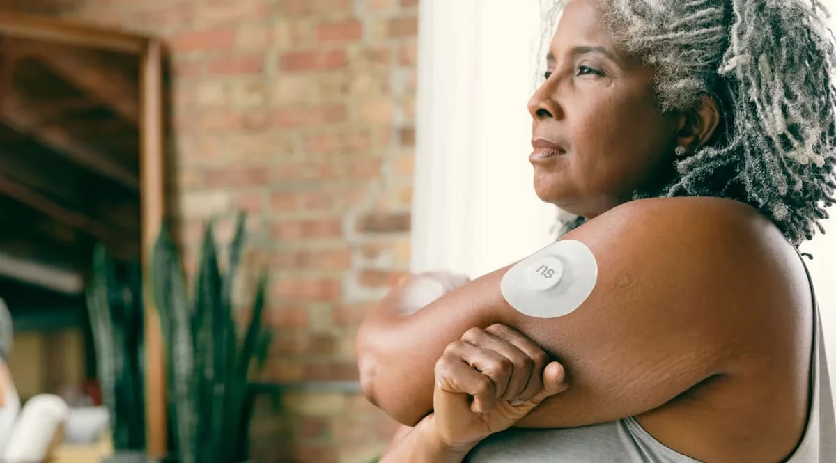 A woman wearing a continuous glucose sensor on her upper arm