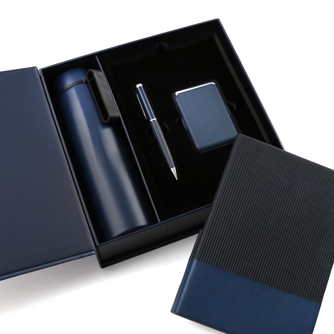Black presentation box containing a dark bottle, notebook, pen and small accessory