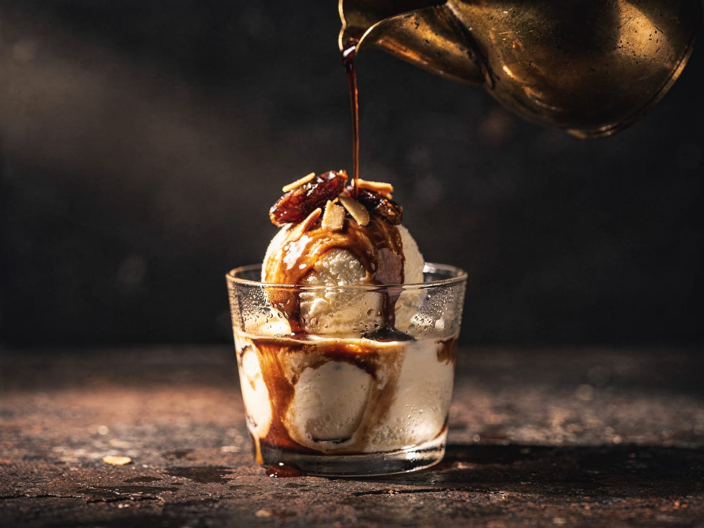 Hot date seed coffee poured from a brass jug over vanilla ice cream topped with chopped dates and almonds