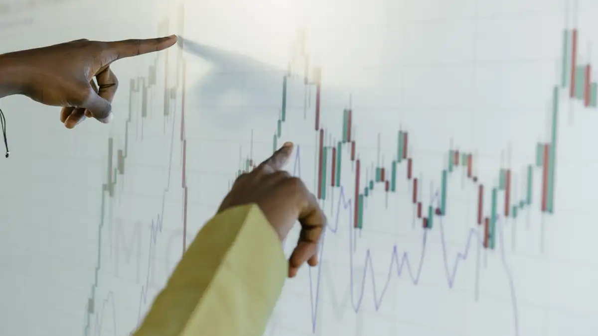 Tangan menunjuk ke grafik saham keuangan di layar digital, menyoroti analisis data dan tren.
