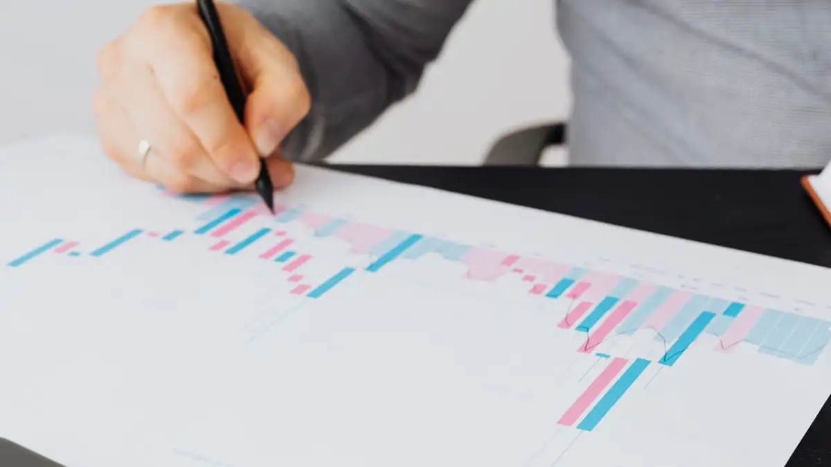 Close-up seorang pria yang menulis di grafik cetak di dalam ruangan, menganalisis data berwarna.