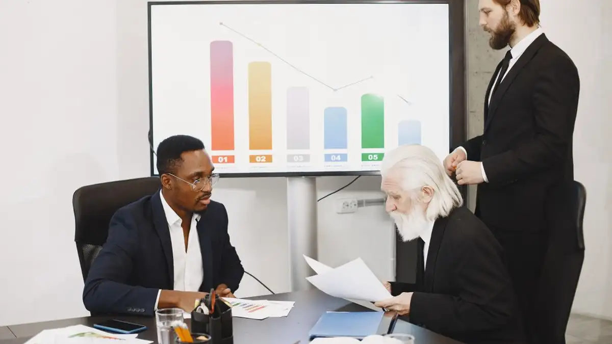 Tiga pengusaha membahas data keuangan di lingkungan kantor modern dengan grafik.
