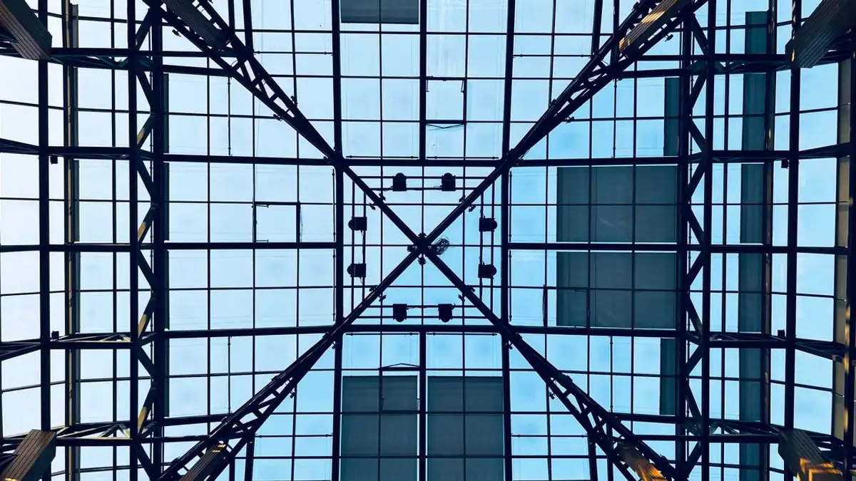 Pemandangan mencolok dari langit atrium kaca yang dibingkai dengan struktur baja dan langit biru yang terlihat.