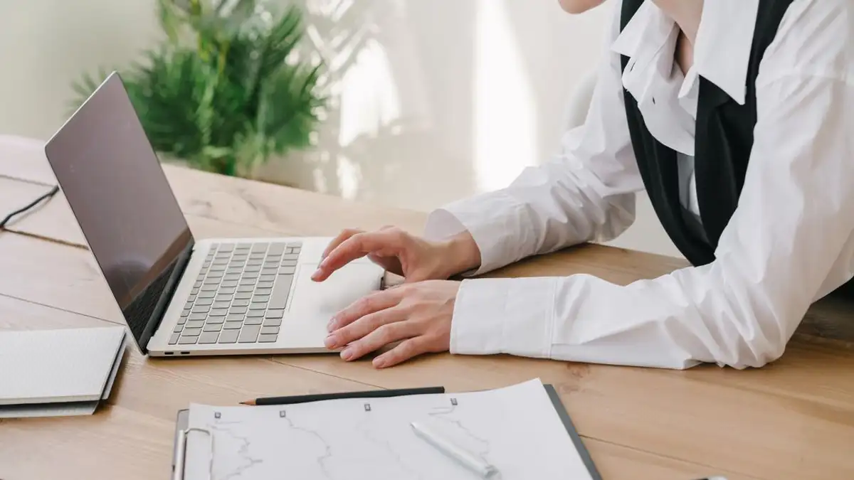Wanita profesional menggunakan laptop di meja kayu dengan perlengkapan kantor.