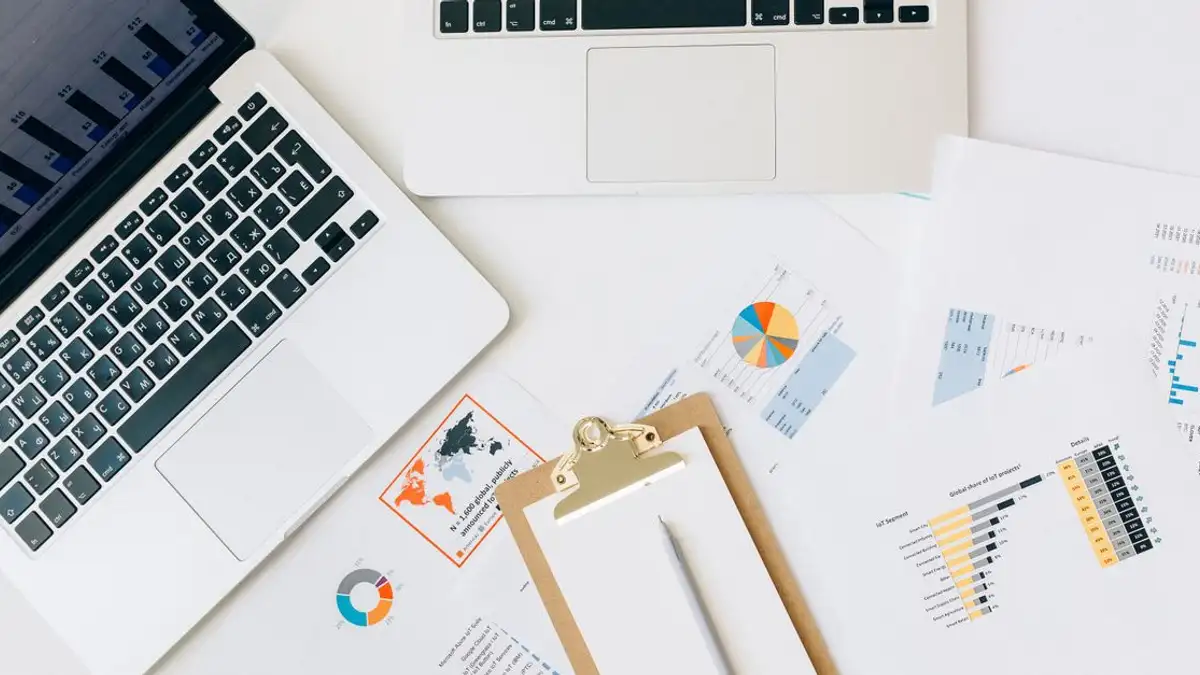 Pandangan dari atas laptop, grafik, dan laporan yang digunakan untuk analisis data di atas meja.
