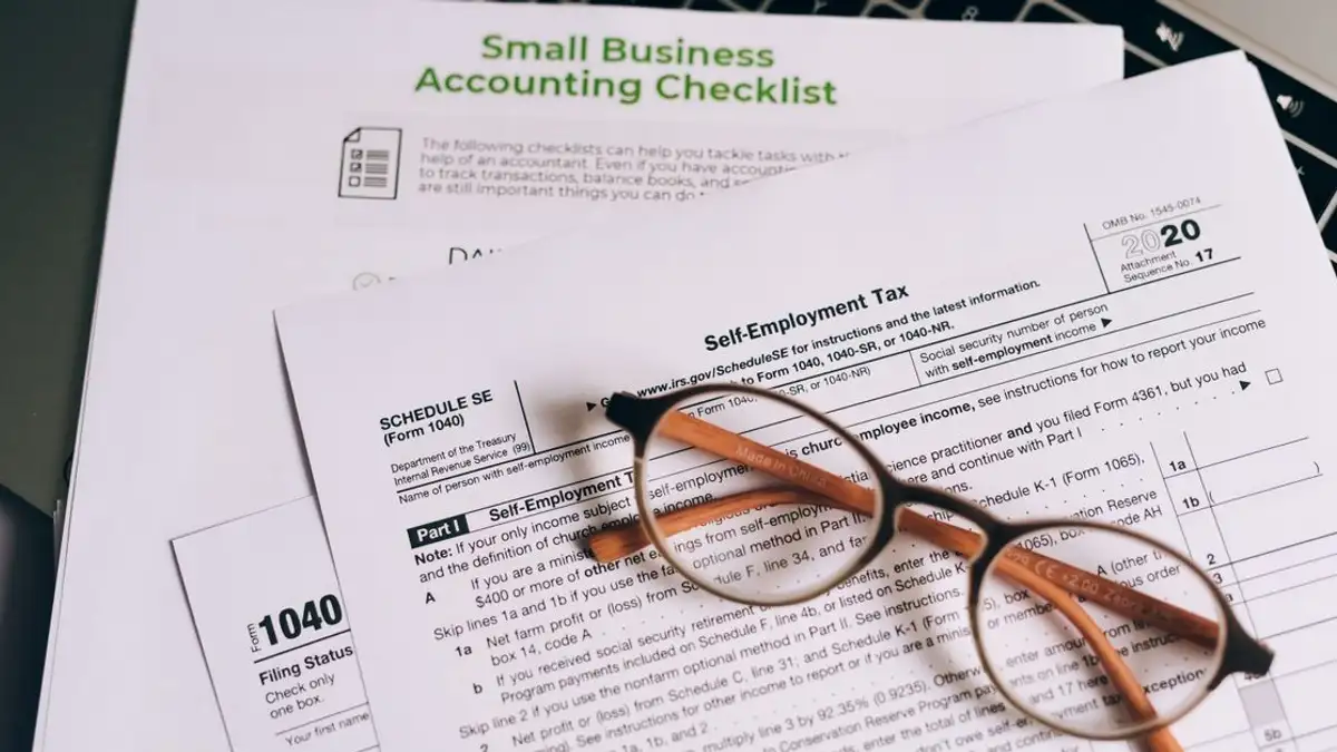 Close-up formulir pajak dan daftar periksa akuntansi bisnis kecil di laptop.