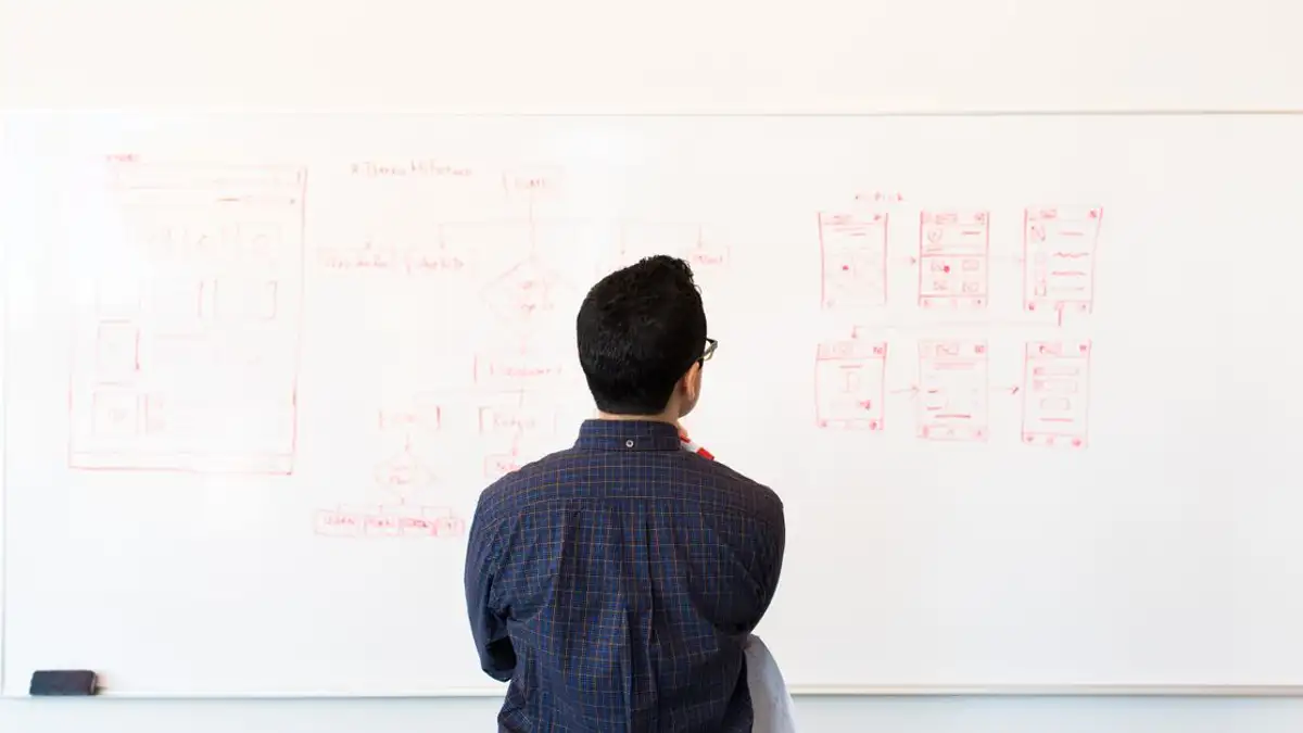 Pria yang berdiri di depan papan putih merencanakan konsep desain UX di lingkungan kantor modern.