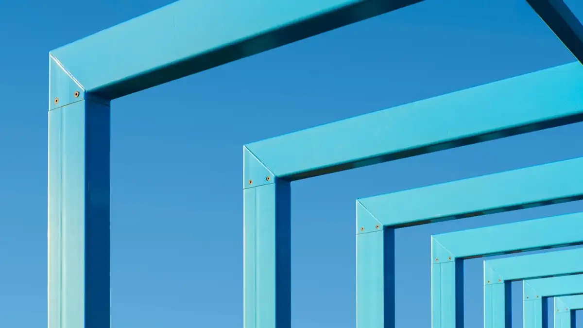 Tampilan abstrak dari bingkai logam biru yang sejajar dengan langit biru cerah, menciptakan pola geometris.
