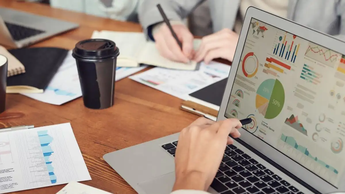 Profesional terlibat dalam pertemuan bisnis, menganalisis data dan grafik di laptop dan kertas.