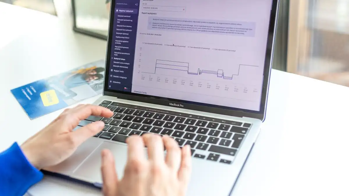 Tangan yang mengetik di laptop menganalisis data bisnis di dekat jendela, menunjukkan teknologi dalam aksi.