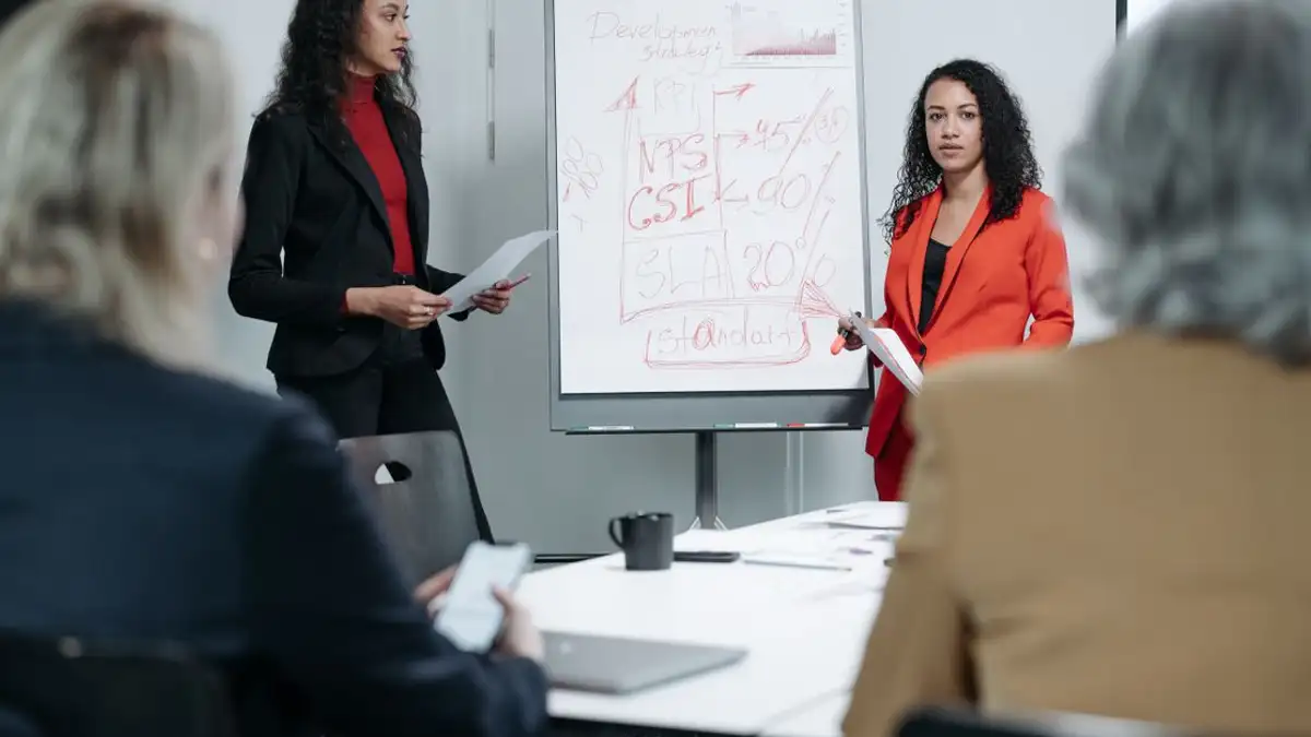 Dua perempuan memimpin pertemuan bisnis dengan fokus pada strategi KPI dan metrik kinerja.