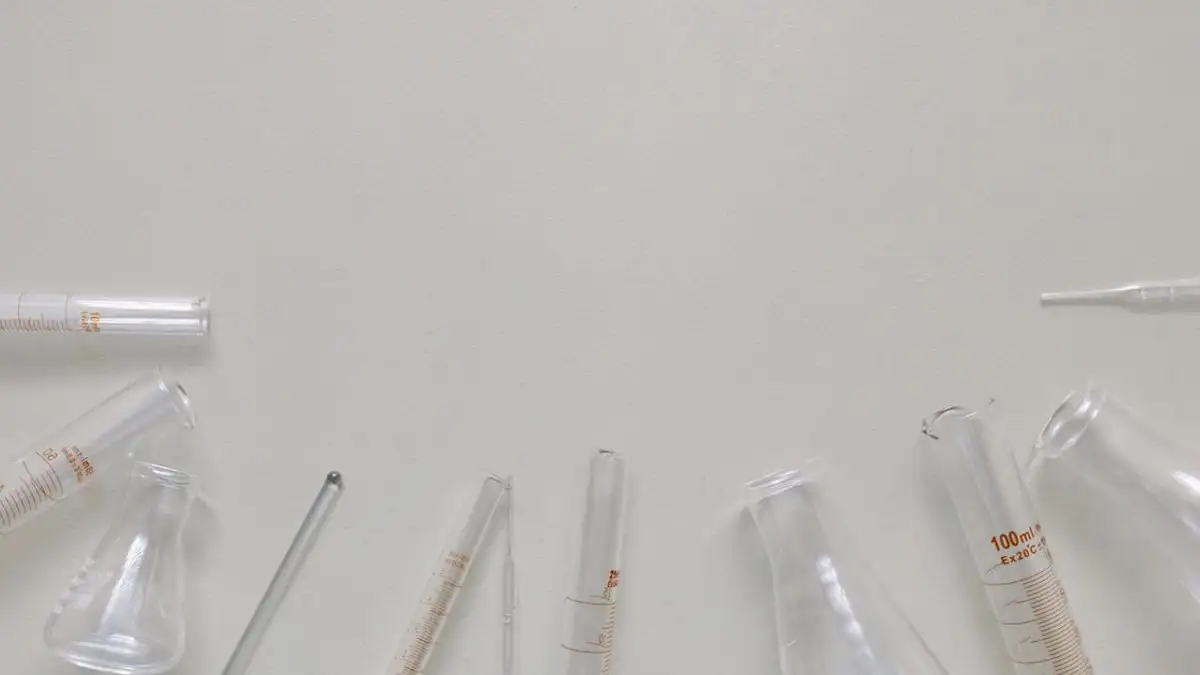 Tampilan datar peralatan laboratorium termasuk gelas ukur dan flask di permukaan netral.