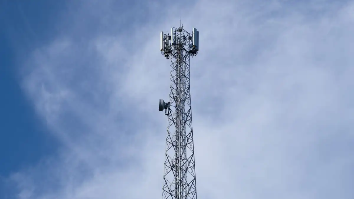 Sebuah menara komunikasi logam yang tinggi berdiri tegak di depan latar belakang langit biru jernih dengan awan yang tersebar.