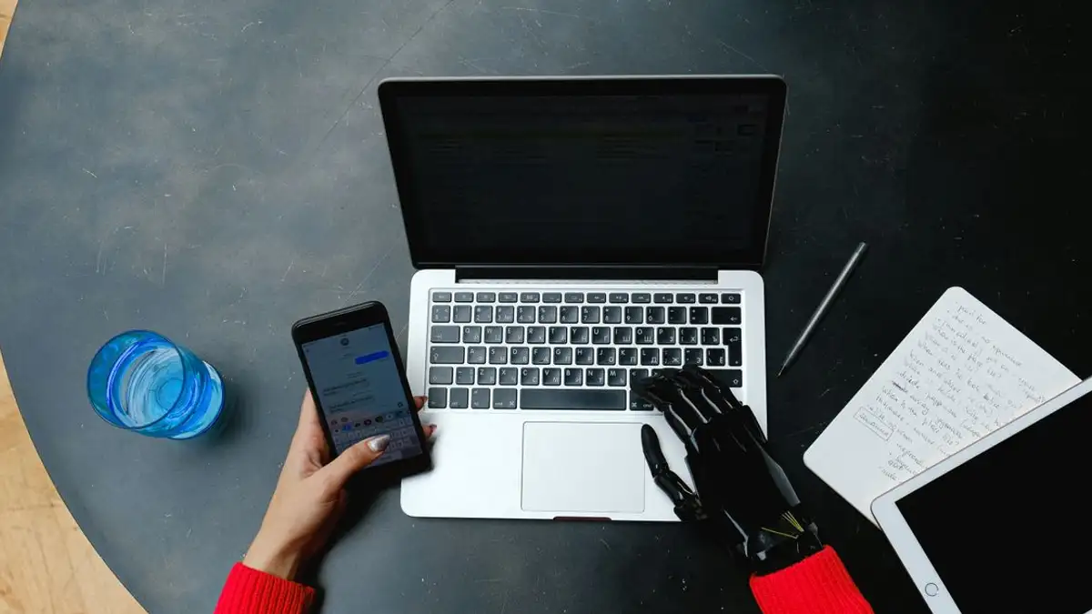 Seseorang menggunakan laptop, smartphone, dan tablet dengan tangan prostetik, menekankan konektivitas digital.