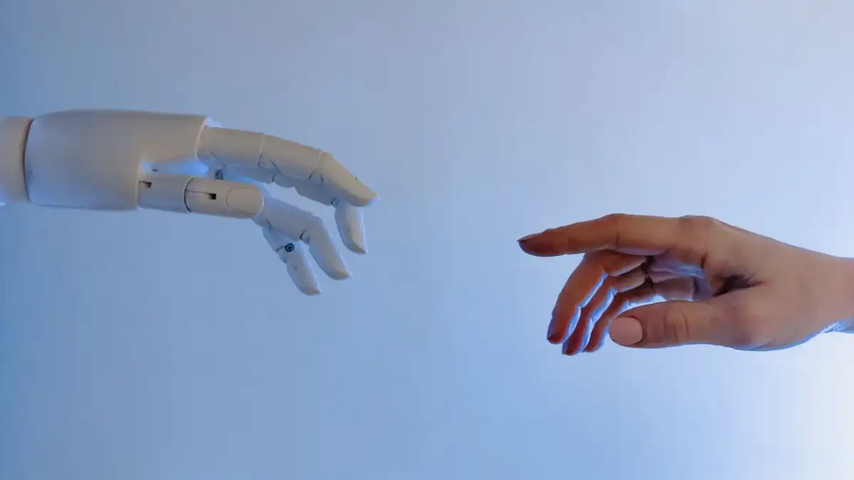 Sebuah tangan manusia yang mengulurkan tangan ke arah tangan robot yang melambangkan teknologi dan koneksi.