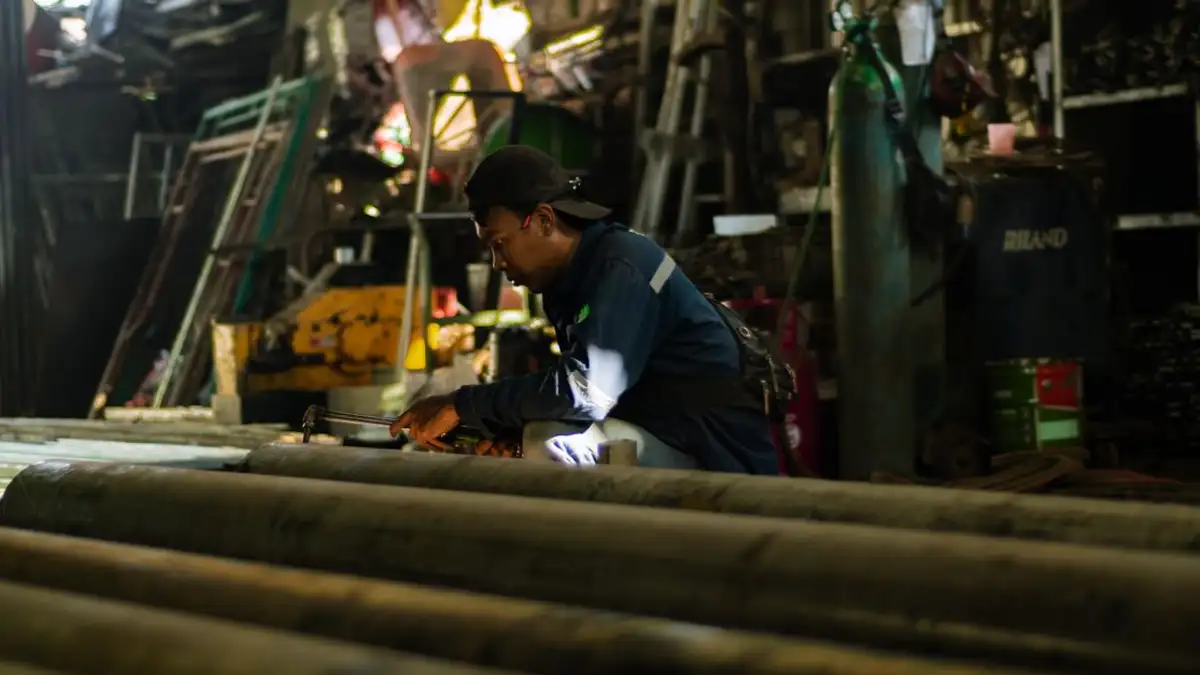 Seorang pengrajin yang fokus bekerja dengan tekun di bengkel industri yang sibuk, menampilkan kerajinan modern.