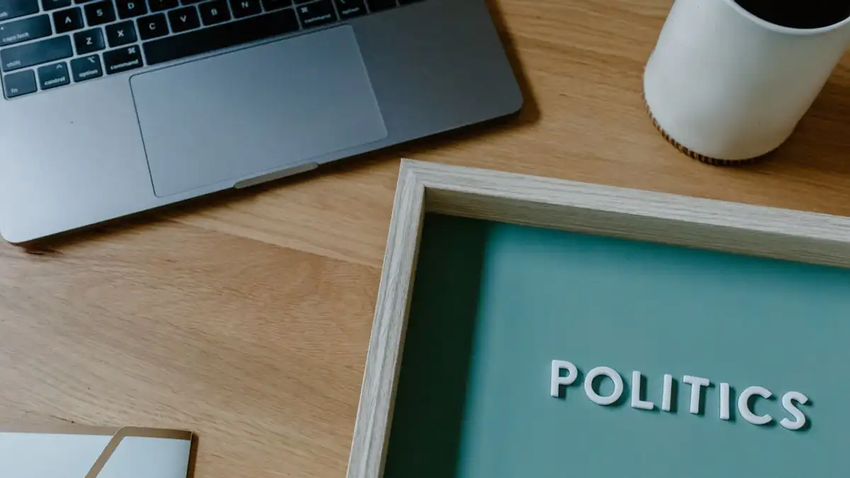 Sebuah ruang kerja kontemporer yang menampilkan laptop, cangkir kopi, dan sebuah tanda dengan kata 'Politik'.