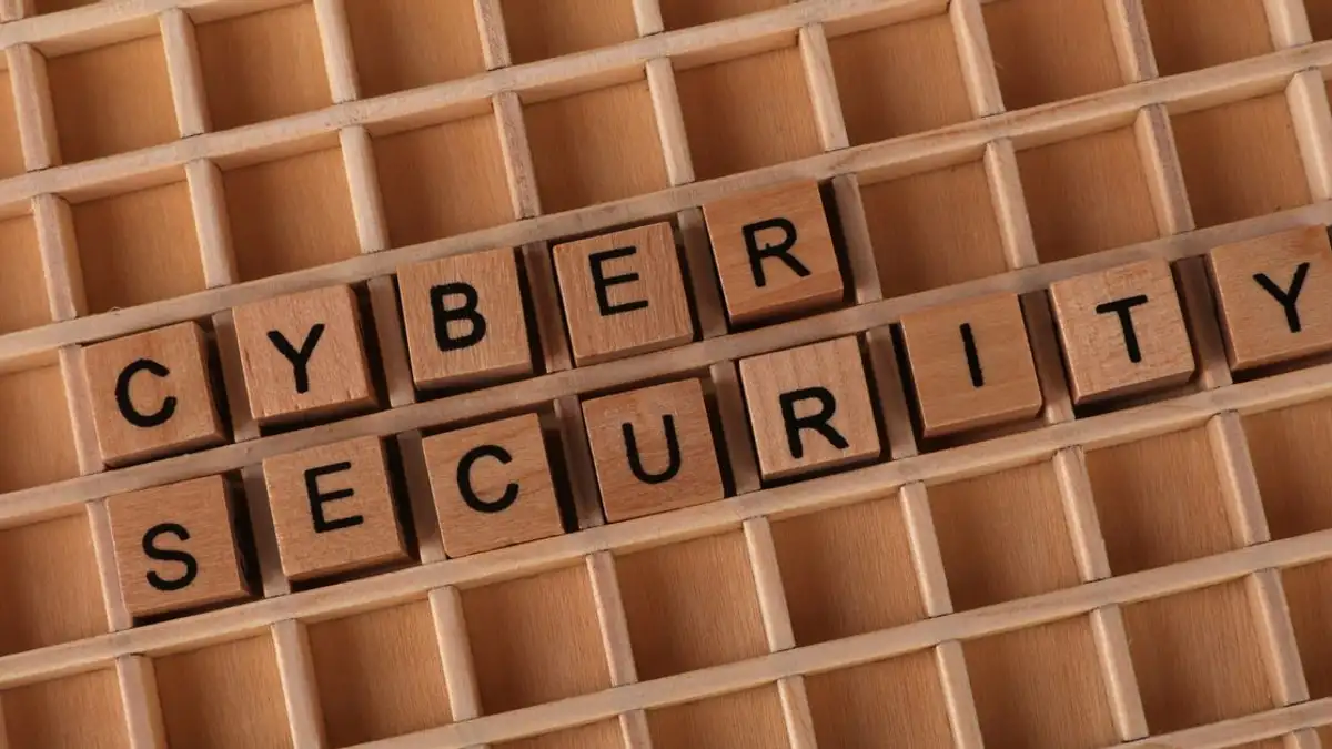 Balok-balok kayu yang membentuk tulisan 'Cyber Security' di atas latar belakang kisi-kisi kayu.