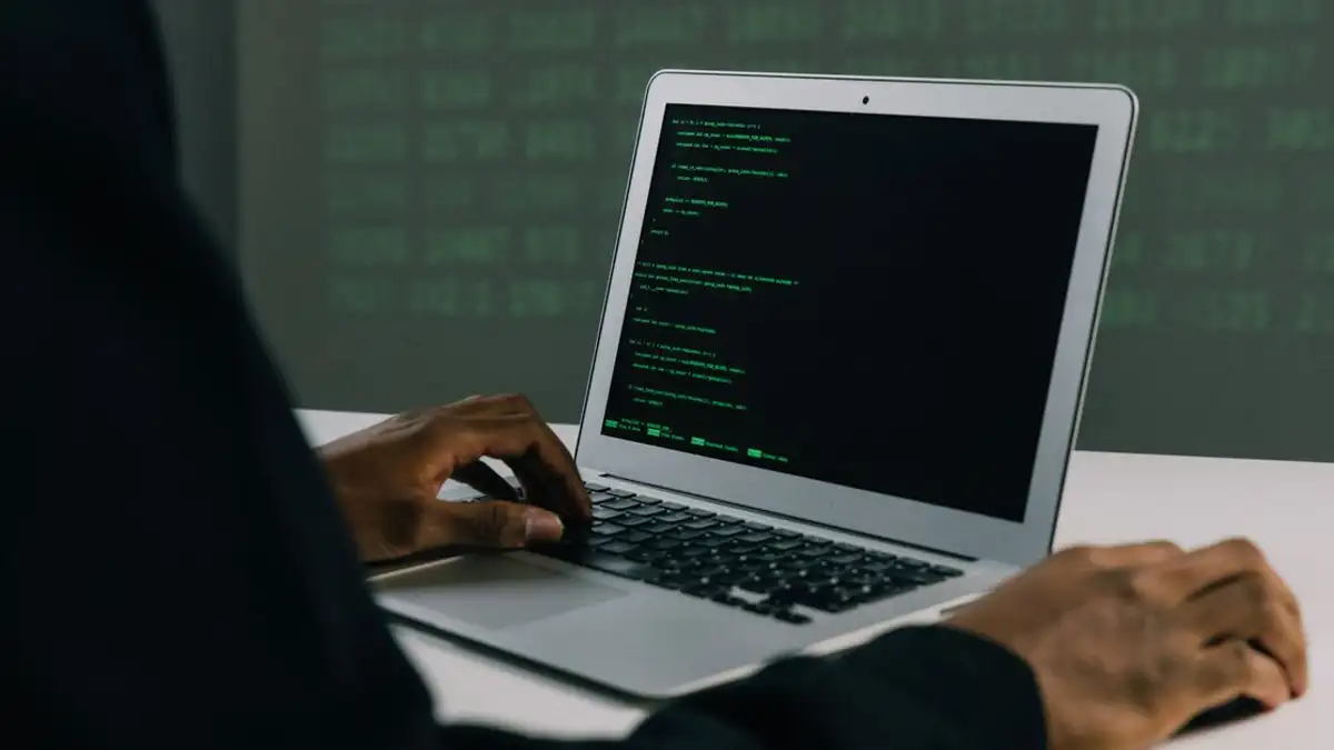 Seorang dewasa yang fokus bekerja di laptop menunjukkan keterampilan keamanan siber dan pengkodean modern di dalam ruangan.