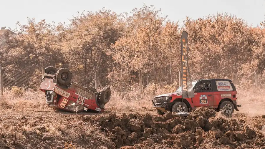 Adegan rally off-road dramatis dengan kendaraan terbalik di tengah dedaunan musim gugur.