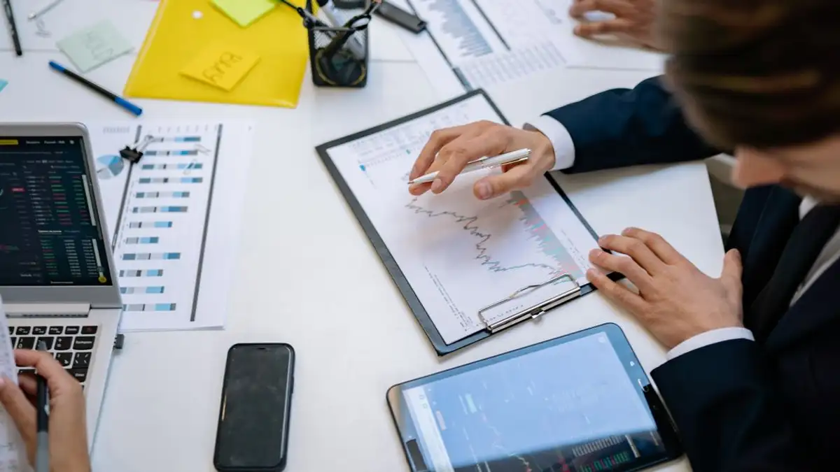 Tim meninjau grafik keuangan dan data digital di tablet dalam pengaturan kantor.