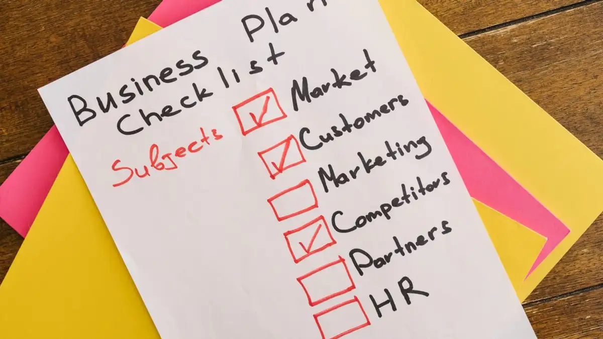 Checklist rencana bisnis yang ditulis tangan di atas meja dengan kertas berwarna-warni yang menunjukkan topik penting untuk startup.