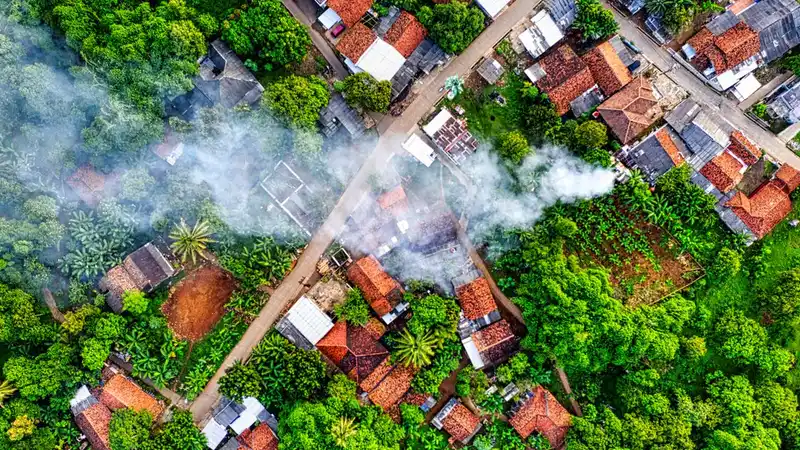 Pandangan drone menangkap lanskap desa hijau dengan asap di Banten, Indonesia.