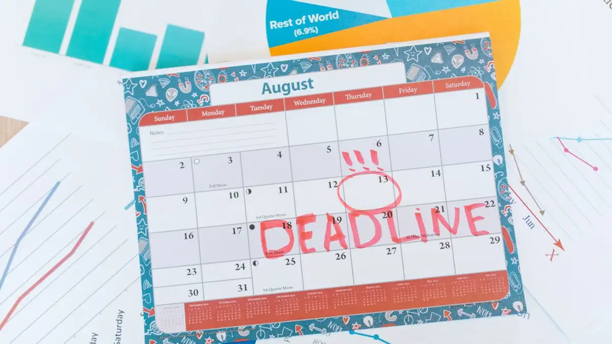 Kalender Agustus yang cerah di atas meja dengan tenggat waktu yang ditandai dengan merah, dikelilingi oleh grafik dan chart.