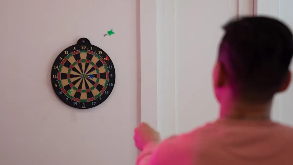 Seseorang mengarahkan pada papan dart di dinding, menunjukkan ketepatan dan fokus.