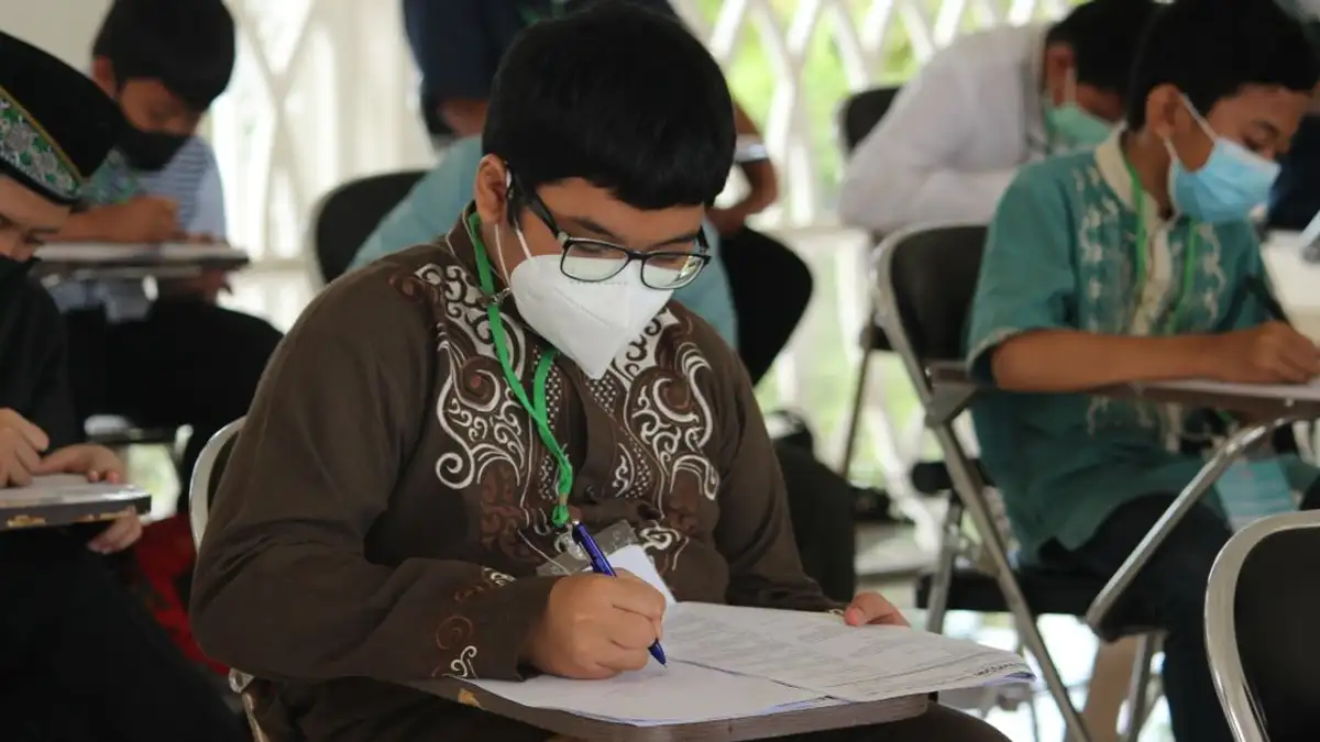 Siswa dengan masker wajah menulis ujian, mewakili normal baru dalam pendidikan selama pandemi COVID-19.