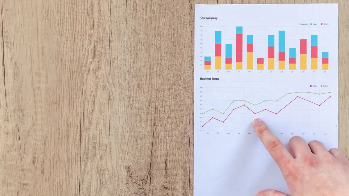 Tangan menganalisis grafik bisnis di meja kayu, fokus pada hasil data dan analisis pertumbuhan.