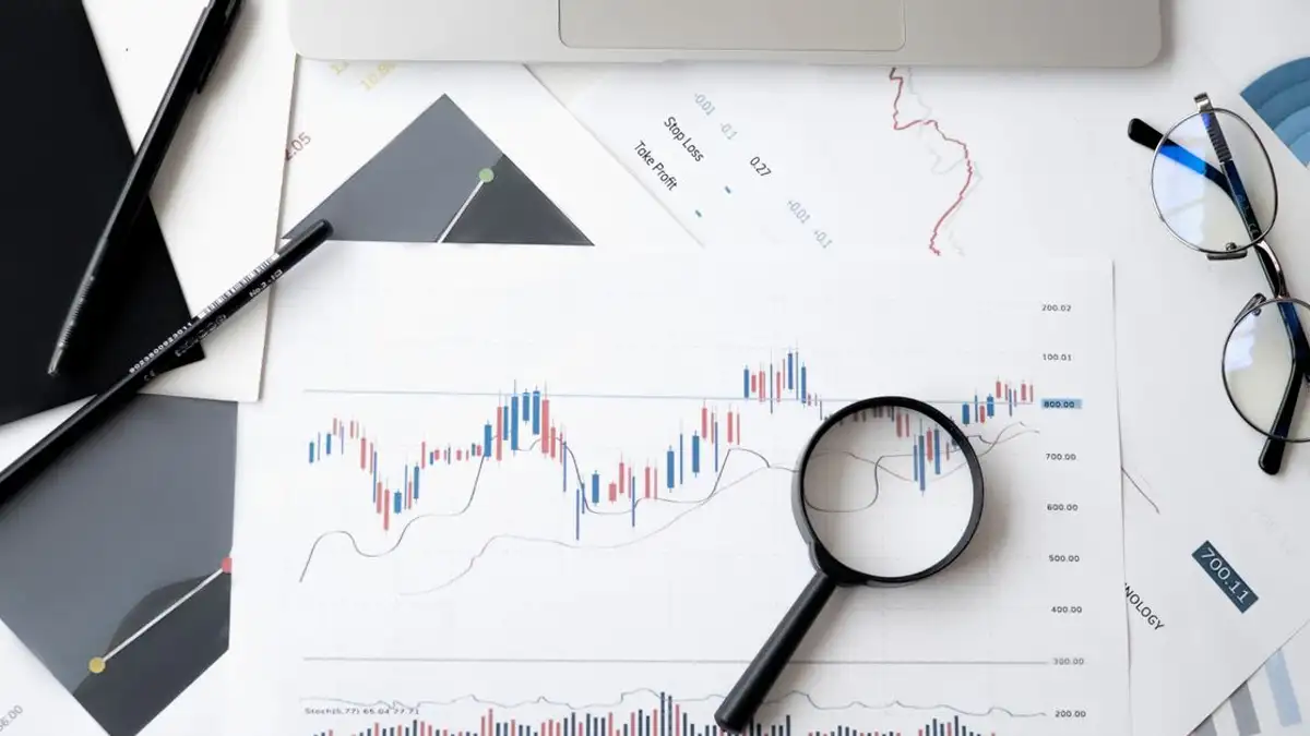 Tampilan datar dokumen analisis pasar saham dengan kaca pembesar, pena, dan kacamata.