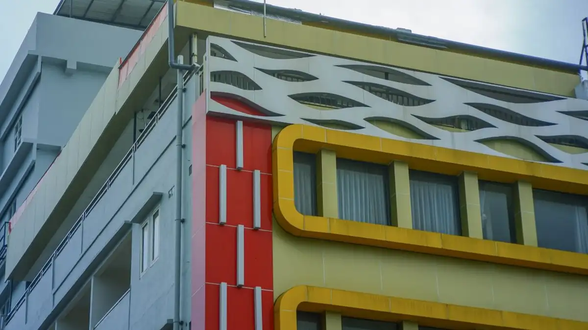 Tampilan dekat fasad bangunan modern yang menampilkan elemen merah, kuning, dan putih di lingkungan perkotaan.