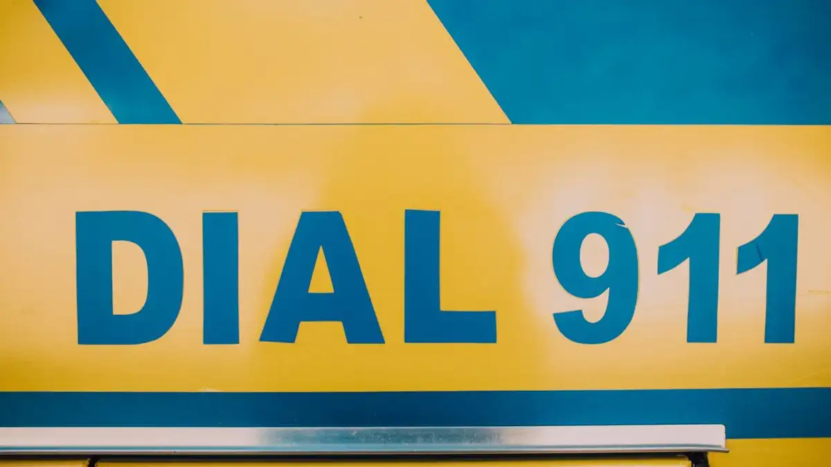 Close-up tanda darurat 'Hubungi 911' pada kendaraan dengan warna kuning dan biru yang mencolok.