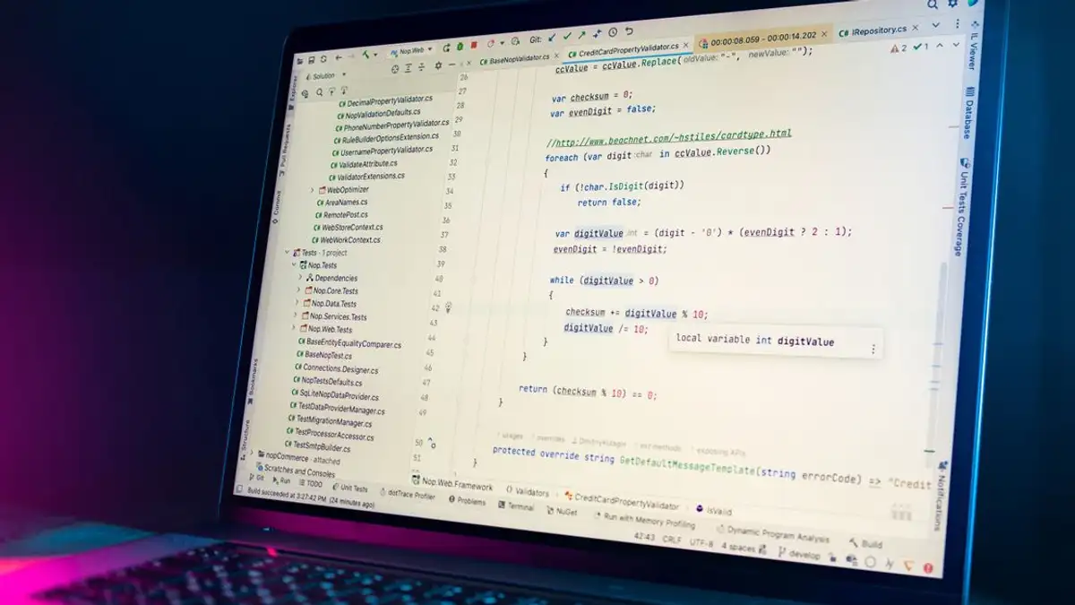 Layar laptop yang menunjukkan editor kode dengan kode pemrograman yang terlihat di lingkungan yang redup.
