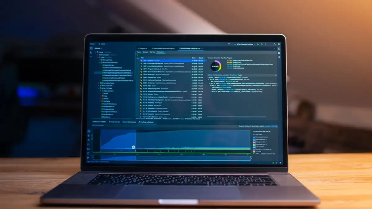 Sebuah laptop yang menampilkan kode di atas meja kayu, dalam ruang kerja yang redup.