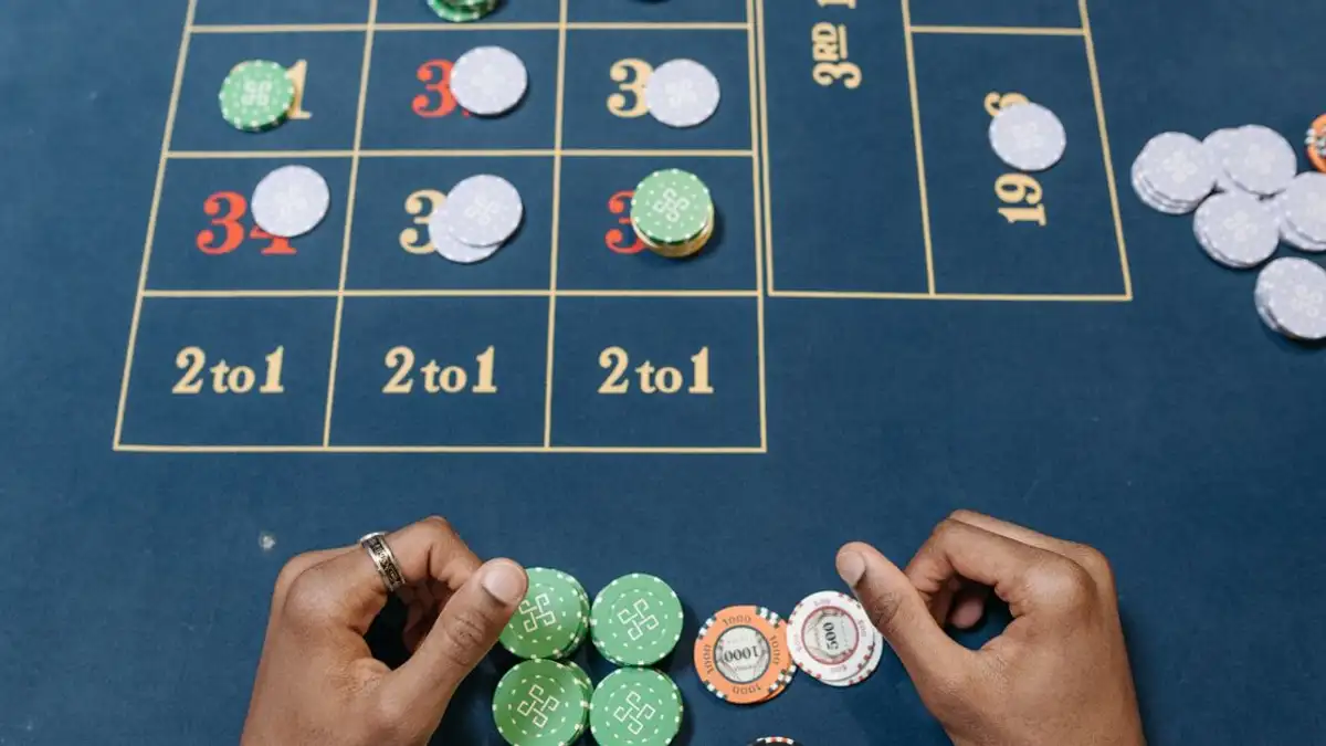 Tangan yang mengatur chip poker di meja permainan kasino yang berwarna-warni, tampak dari atas.