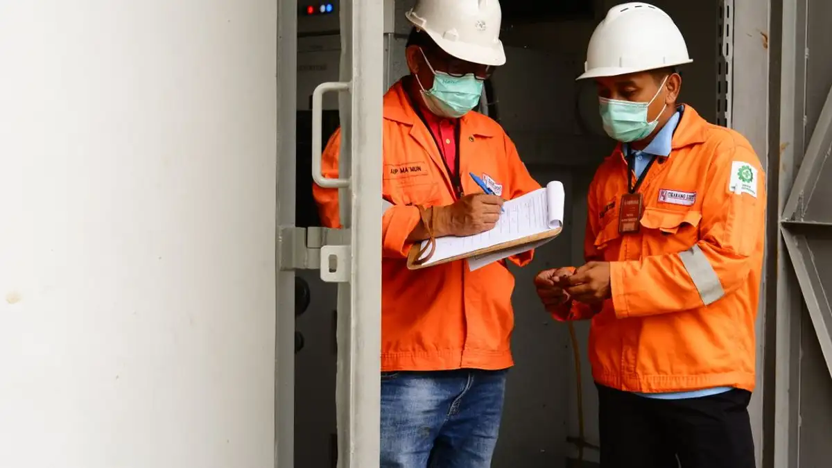 Dua pekerja konstruksi dalam perlengkapan keselamatan membahas rencana di pintu masuk situs.
