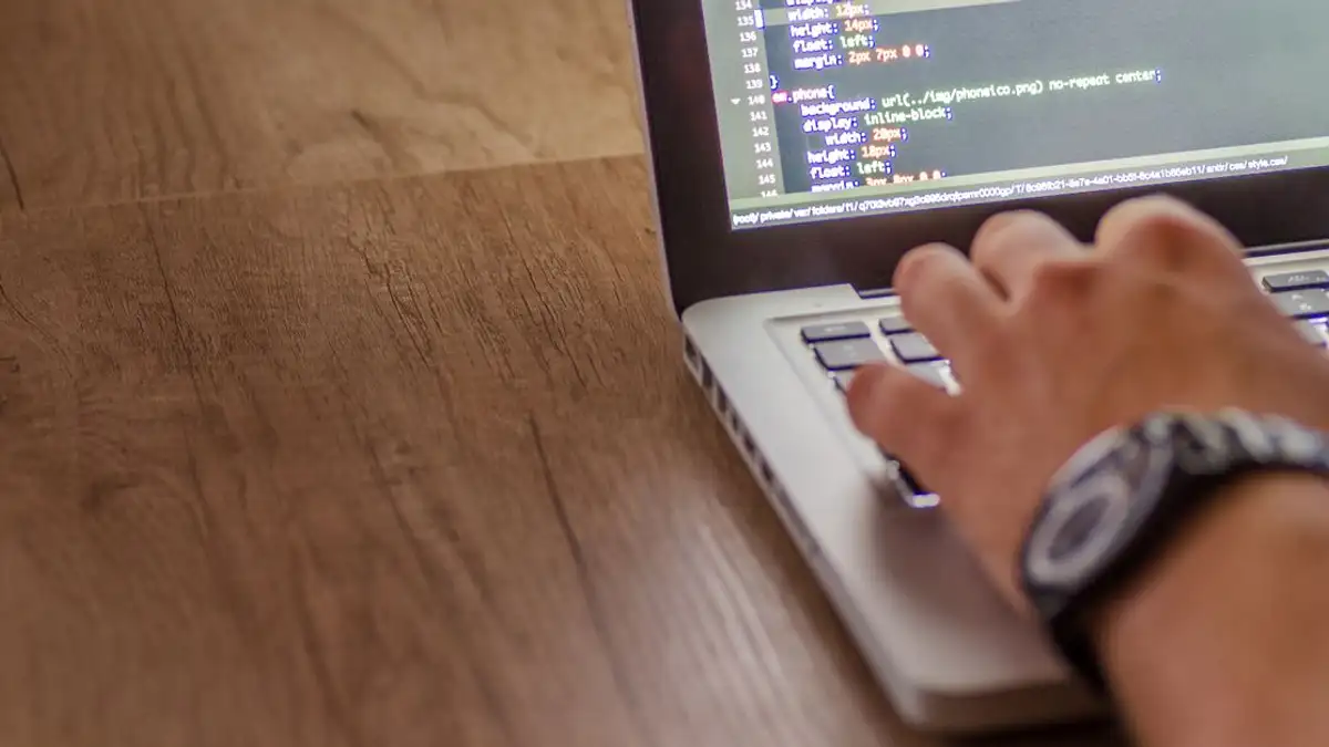 Close-up seseorang yang sedang mengkode di laptop, menampilkan konsep pengembangan web dan pemrograman.