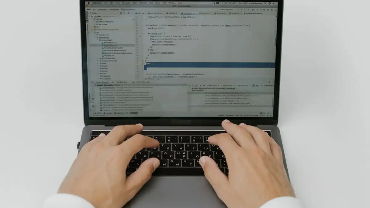 Close-up tangan yang sedang melakukan pengkodean di laptop, menampilkan pengembangan perangkat lunak dalam aksi.