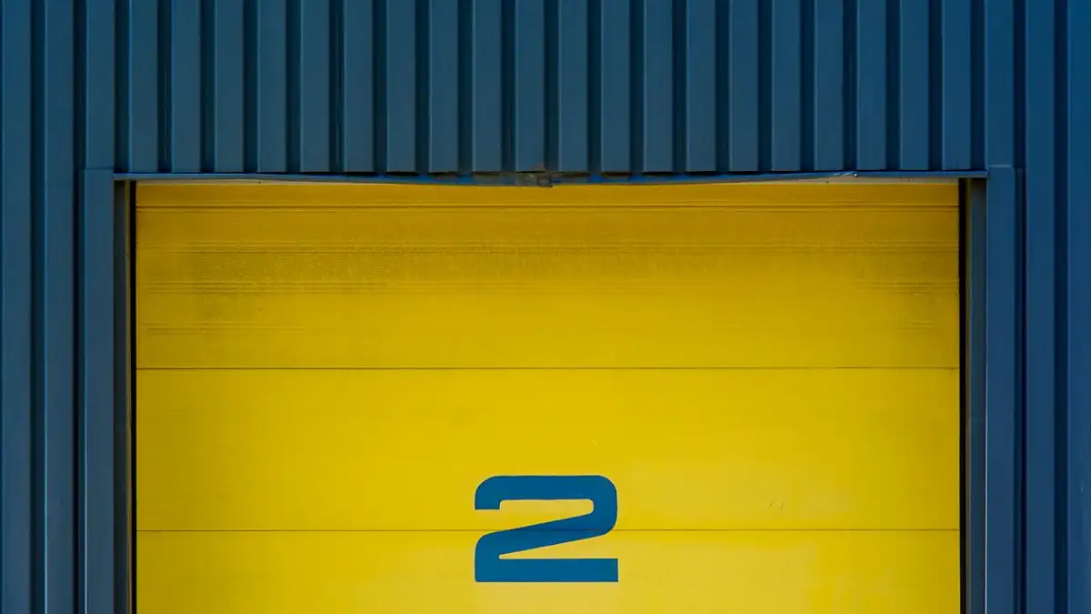 Close-up pintu industri kuning dengan nomor 2, terletak di eksterior gedung modern.
