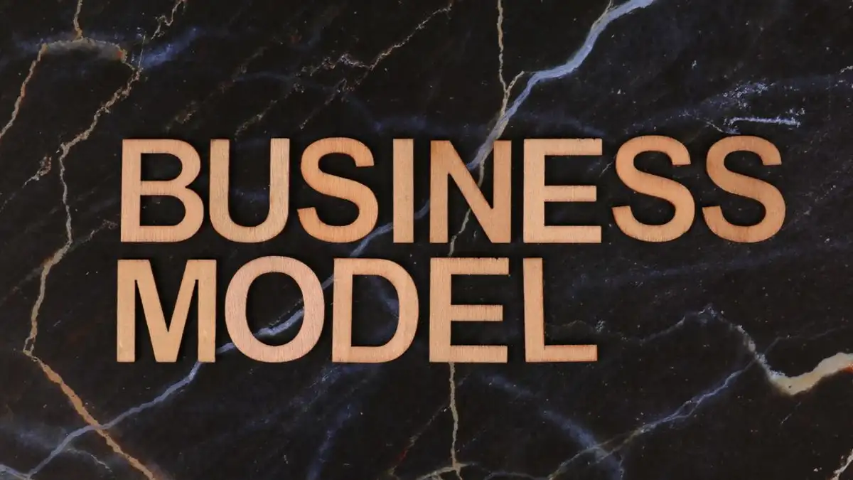 Huruf-huruf kayu yang mengeja 'BUSINESS MODEL' di atas latar belakang marmer gelap.
