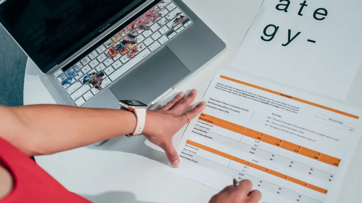 Tampilan dari atas tangan di atas kertas strategi bisnis dengan laptop, menyoroti perencanaan modern.