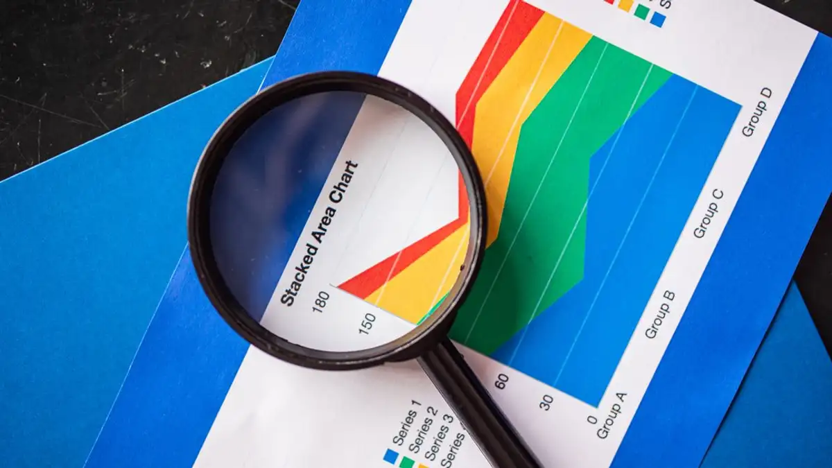 Kaca pembesar yang menyoroti grafik area tumpuk untuk analisis bisnis.