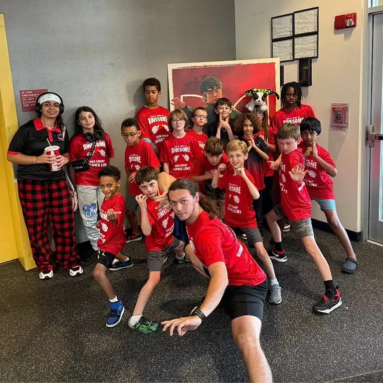 Group of children and instructors in red "Awesome" shirts posing with martial arts stances at Global Summer Camp.