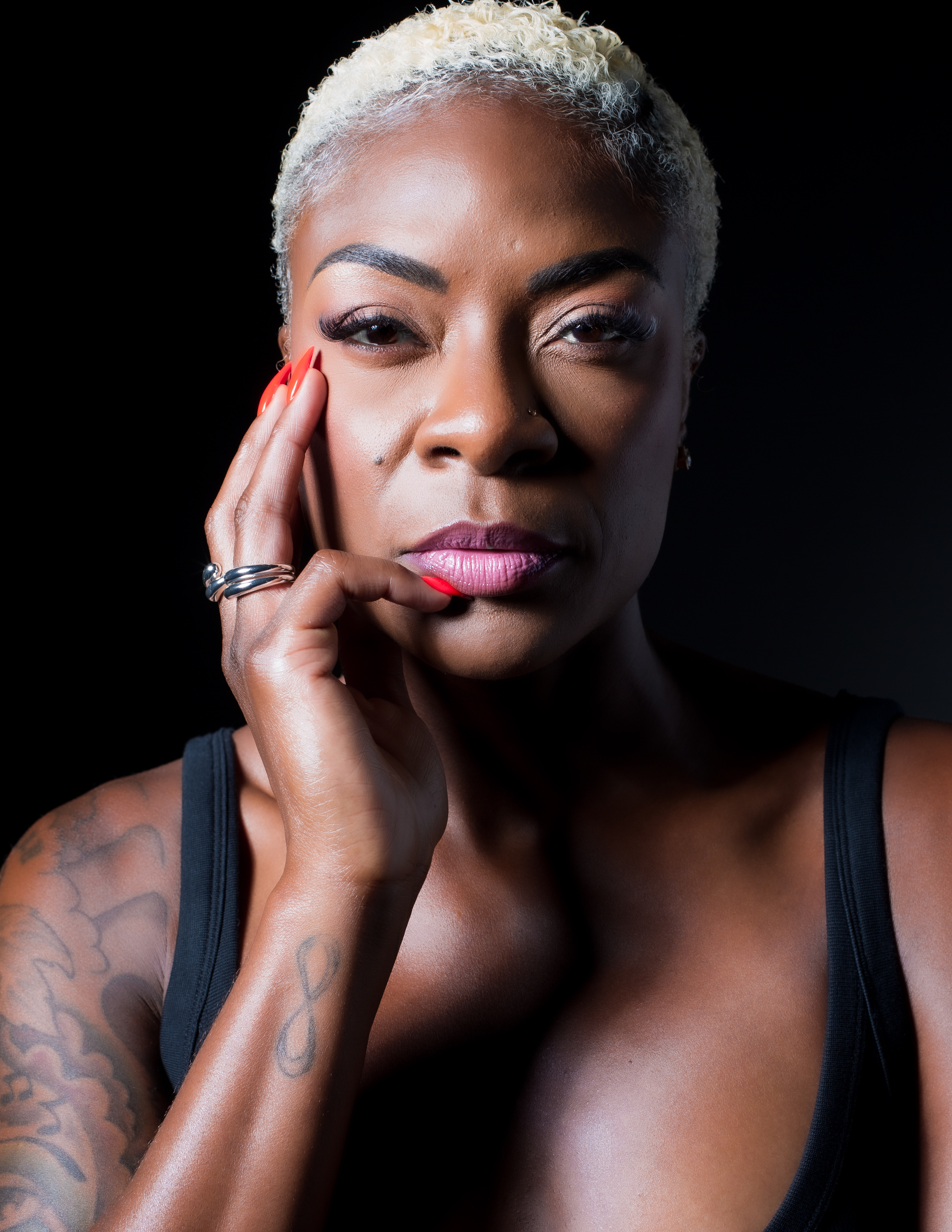 Portrait of woman with white pixie cut hair and pink lipstick on black background.