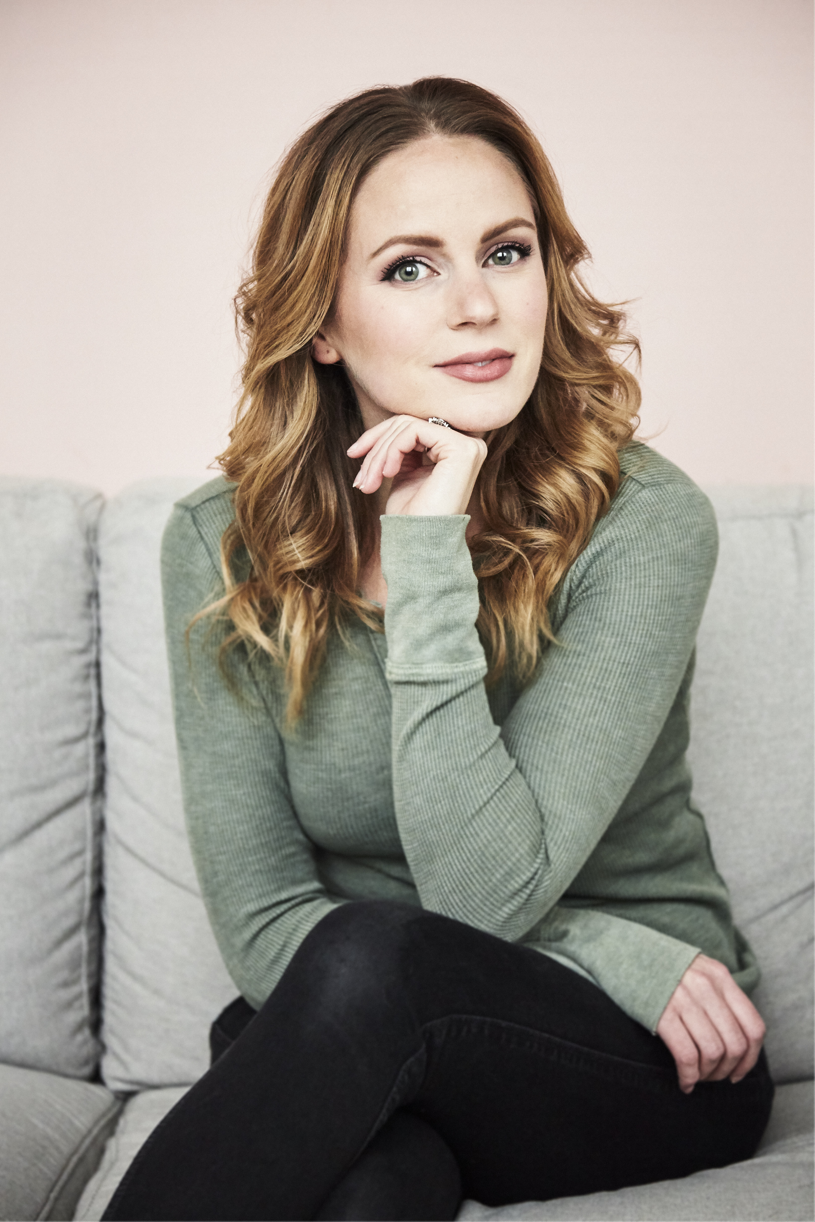Woman with shoulder-length wavy auburn hair wearing green sweater and smiling.