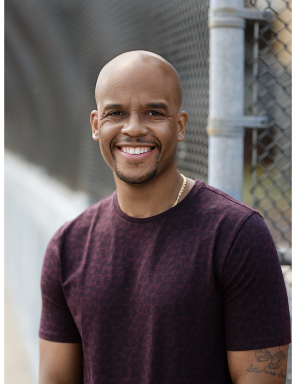 Man with warm smile wearing purple t-shirt.