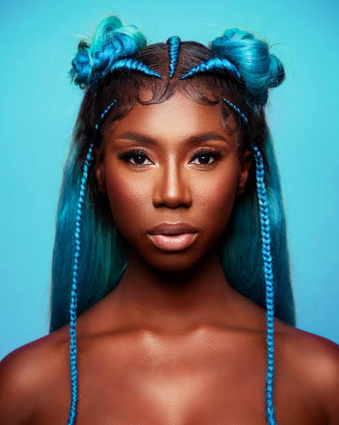 Woman with bright blue braids and blue tulle against turquoise background.