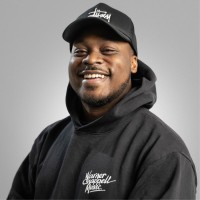 Man wearing black hoodie and cap, smiling warmly.